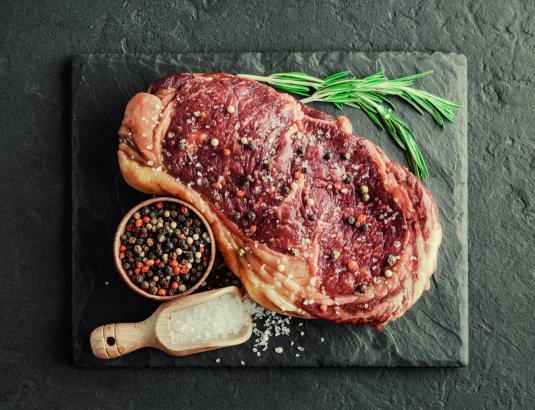 Ein Steak mit buntem Pfeffer liegt vorbereitet auf einer Platte – bereit zum Grillen.